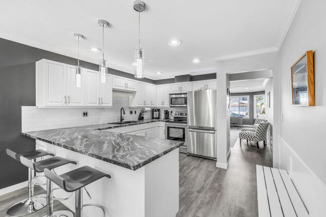 Kitchen featuring a sink, appliances with stainless steel finishes, a peninsula, crown molding, and dark stone counters | Image 12