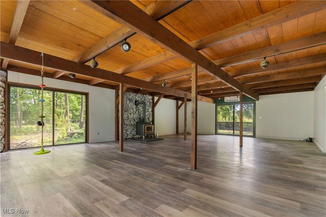 Unfurnished living room with rail lighting, wooden ceiling with exposed beams, wood finished floors, a wood stove, and baseboards | Image 17