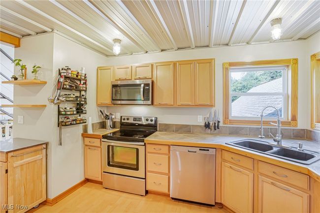 Kitchen featuring appliances with stainless steel finishes, light brown cabinetry, tile countertops, light wood-style flooring, and open shelves | Image 15