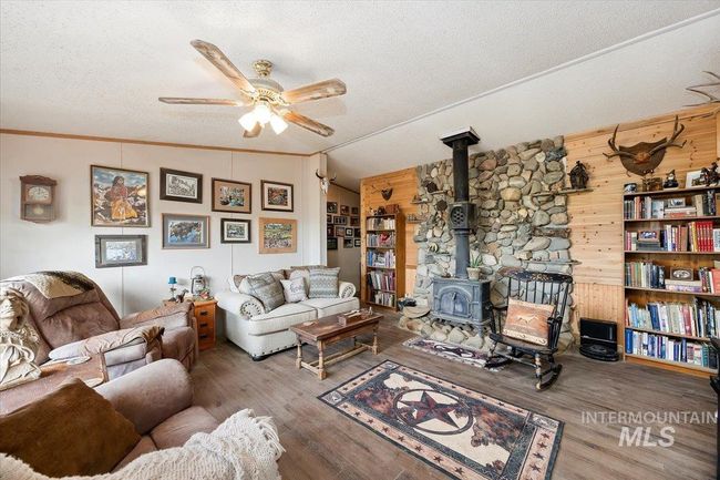 Living area with a wood stove, ceiling fan, a textured ceiling, wood walls, and wood finished floors | Image 14