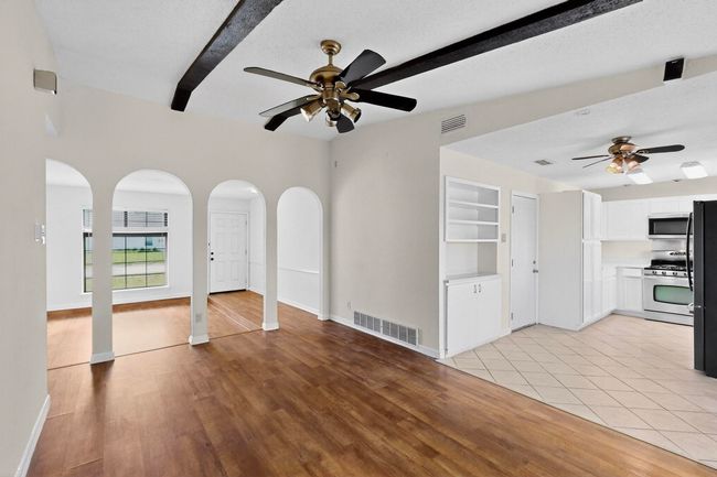 Unfurnished living room with arched walkways, a ceiling fan, beam ceiling, light wood-type flooring, and a textured ceiling | Image 8