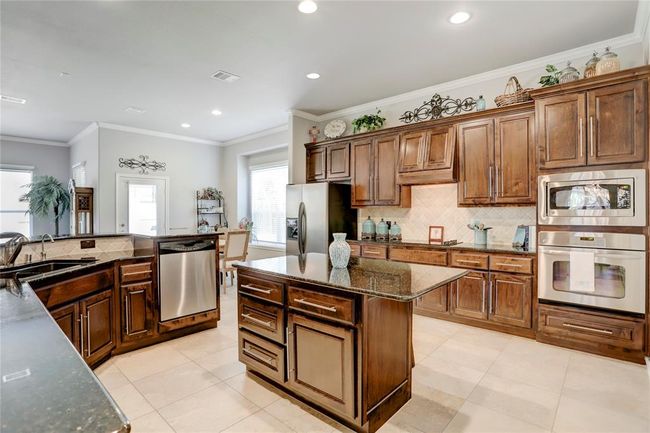 This kitchen features rich wooden cabinetry, granite countertops, stainless steel appliances, and a central island. | Image 15