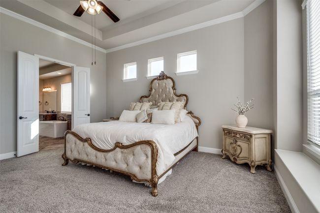 Carpeted bedroom with crown molding, a tray ceiling, ceiling fan, and ensuite bathroom | Image 17