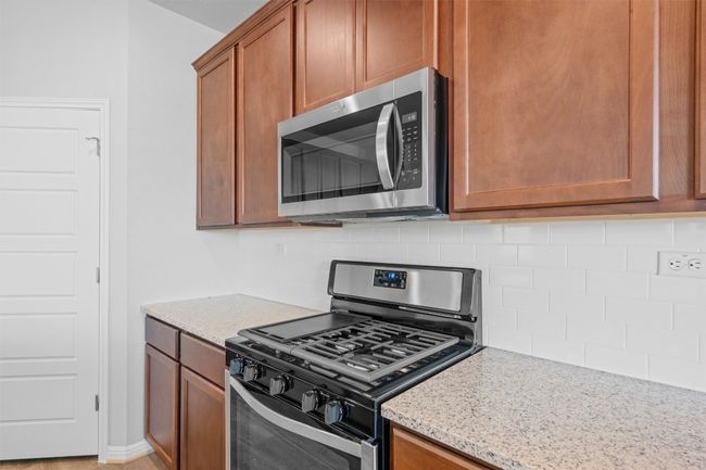 Kitchen with appliances with stainless steel finishes, backsplash, light stone counters, and brown cabinetry | Image 11