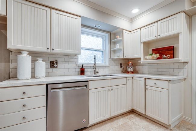 This kitchen features classic white cabinetry, complemented by a modern subway tile backsplash. It includes a stainless steel dishwasher, ample counter space. The window above the sink provides natural light, enhancing the bright and welcoming atmosphere. | Image 13