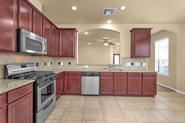 An undermount sink overlooks the breakfast bar, which seamlessly connects the kitchen to the family room—making it perfect for casual meals or lively conversations. Tile flooring and recessed lighting complete this bright, inviting space. | Image 10