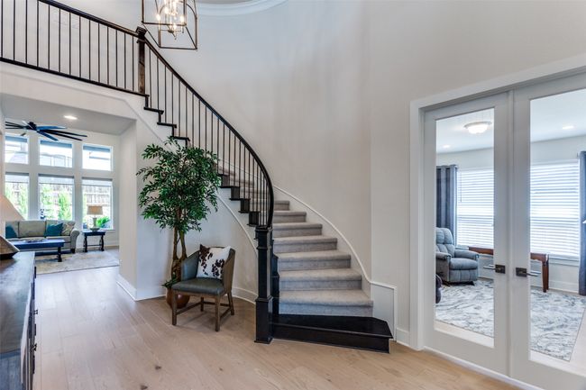 Stairs featuring a towering ceiling, healthy amount of natural light, wood finished floors, a chandelier, and a ceiling fan | Image 6