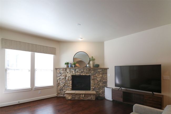 Living room with a stone fireplace, wood finished floors, and baseboards | Image 5