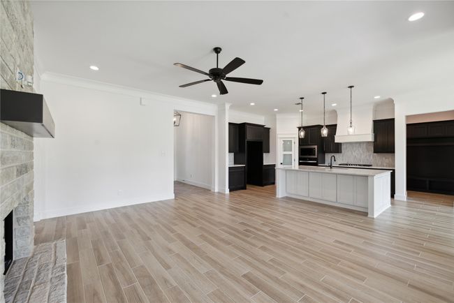 Kitchen with a stone fireplace, tasteful backsplash, an island with sink, ceiling fan, and light wood-type flooring | Image 10