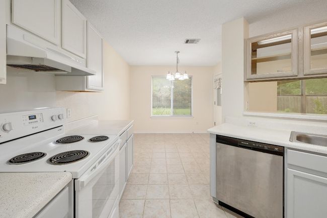 Kitchen with white electric stove, stainless steel dishwasher, under cabinet range hood, a chandelier, and light countertops | Image 13