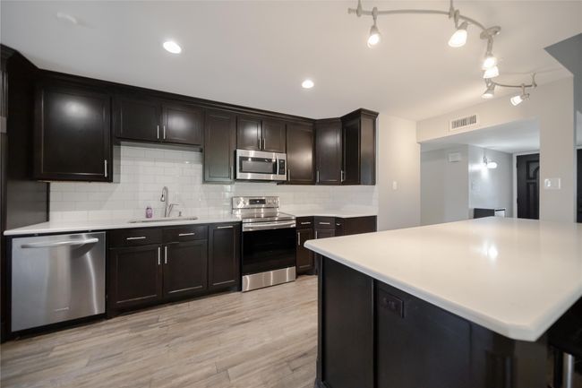 Kitchen with stainless steel appliances, decorative backsplash, light countertops, and light wood-type flooring | Image 10