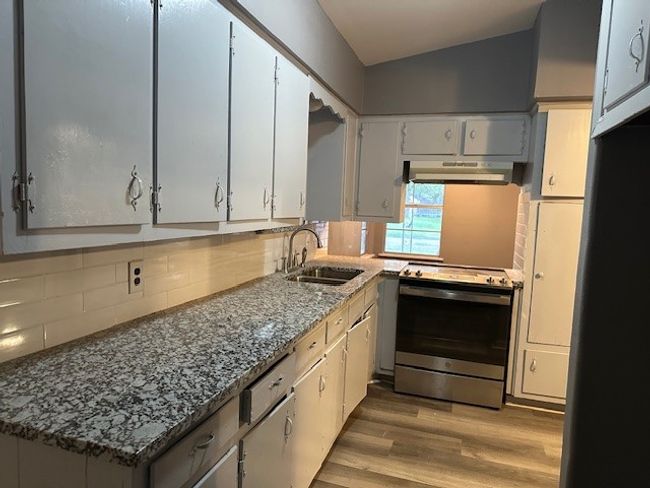 Kitchen with stainless steel electric stove, a sink, light wood-style floors, under cabinet range hood, and fridge | Image 6