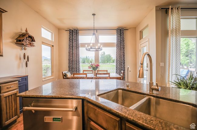 Kitchen featuring stainless steel dishwasher, a chandelier, a sink, decorative light fixtures, and dark stone counters | Image 11