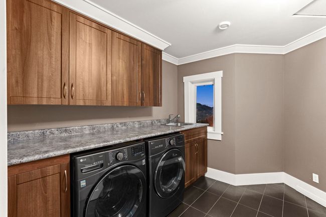 Clothes washing area with crown molding, a sink, washing machine and clothes dryer, cabinet space, and dark tile patterned flooring | Image 30