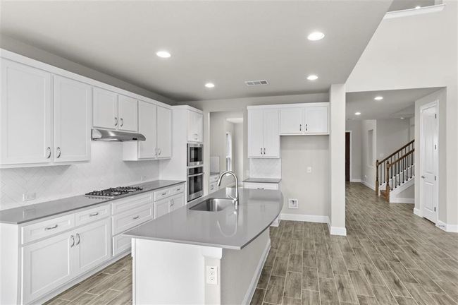 Kitchen with a sink, stainless steel gas cooktop, under cabinet range hood, light wood-type flooring, and baseboards | Image 10