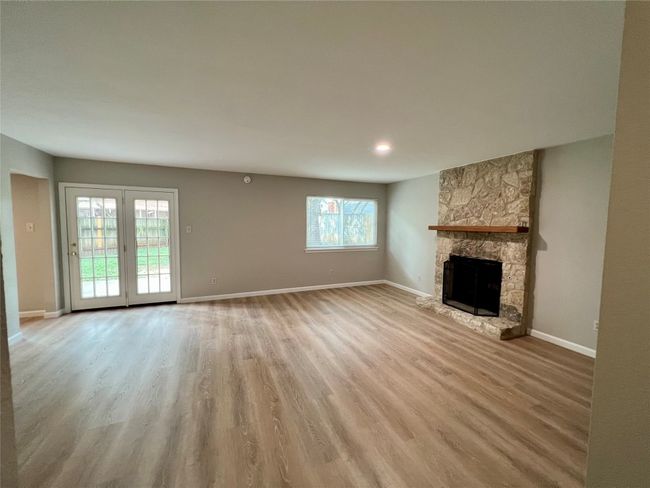 Unfurnished living room with light wood-type flooring, a stone fireplace, and baseboards | Image 5