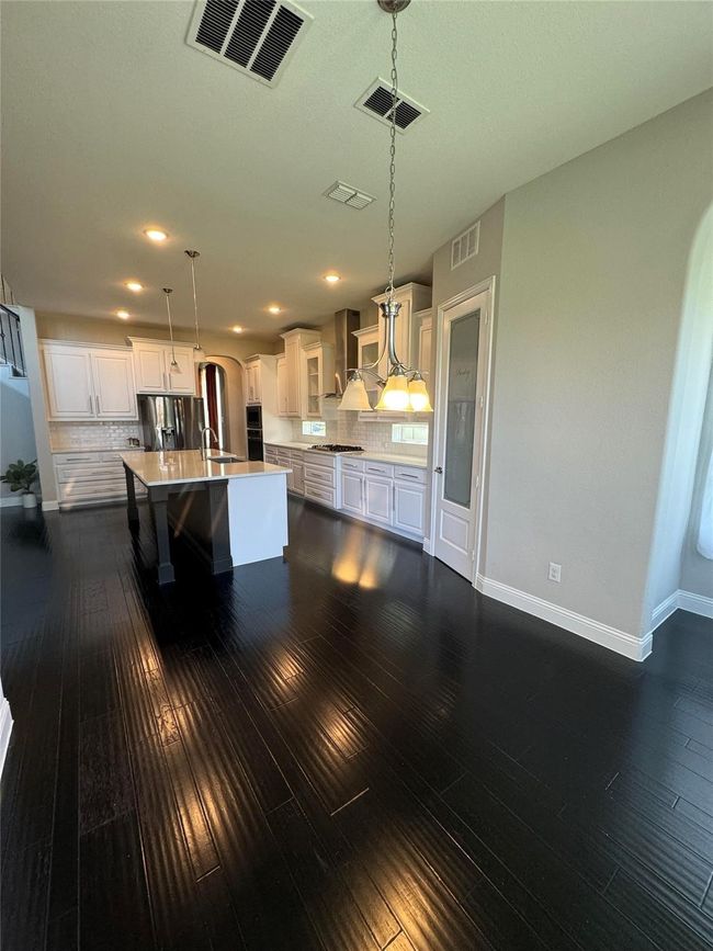 Kitchen with stainless steel appliances, dark wood-style flooring, a kitchen island with sink, light countertops, and backsplash | Image 16