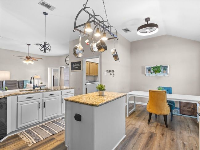 Kitchen with washer and dryer, wood finished floors, a kitchen island, ceiling fan, and vaulted ceiling | Image 10