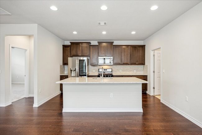 Kitchen with dark brown cabinets, a kitchen island with sink, stainless steel appliances, tasteful backsplash, and visible vents | Image 9