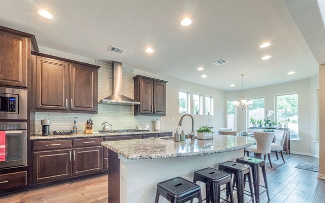 The glorious kitchen features granite countertops, a large kitchen island and breakfast bar, stainless appliances, a walk-in pantry, and tons of cabinet space. | Image 6