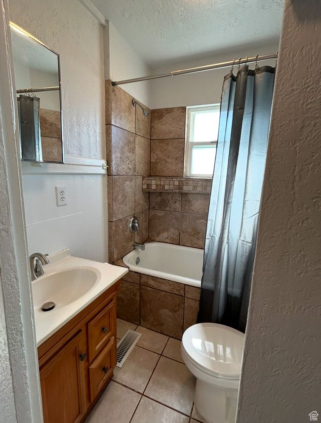 Bathroom with a textured ceiling, tiled shower / bath combo, tile patterned floors, vanity, and a textured wall | Image 8