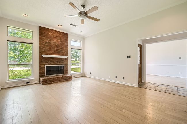 Unfurnished living room featuring ceiling fan, a textured ceiling, light wood-style floors, a brick fireplace, and ornamental molding | Image 11