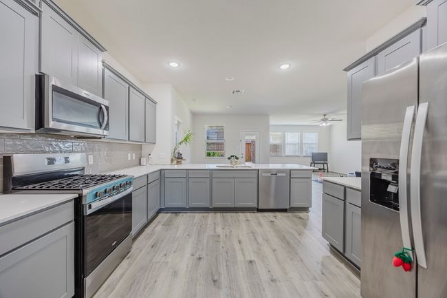 Kitchen featuring appliances with stainless steel finishes, gray cabinetry, a peninsula, light countertops, and light wood finished floors | Image 8