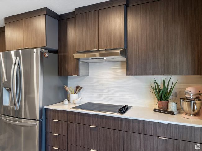 Kitchen featuring stainless steel fridge, black electric stovetop, range hood, decorative backsplash, and light countertops | Image 16