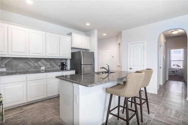 Kitchen featuring freestanding refrigerator, arched walkways, a kitchen breakfast bar, dark stone counters, and white cabinetry | Image 26