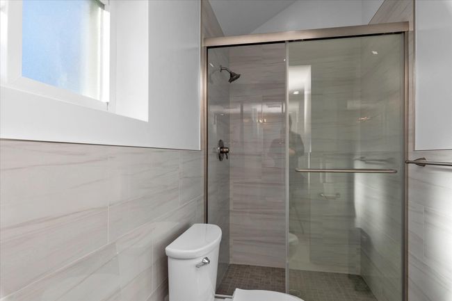Bathroom with toilet, tile walls, and a shower with shower door | Image 11