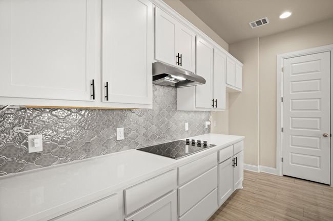 Kitchen with light wood-style flooring, under cabinet range hood, visible vents, black electric stovetop, and white cabinets | Image 10