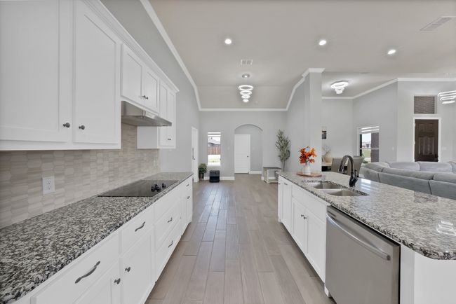 Kitchen with dishwasher, black electric cooktop, under cabinet range hood, arched walkways, and crown molding | Image 6