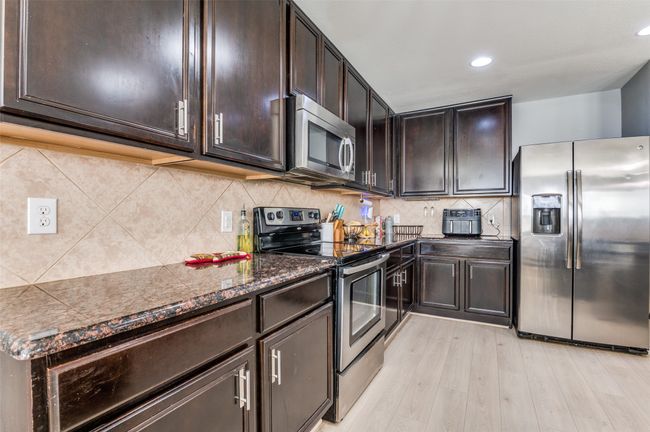 Kitchen with appliances with stainless steel finishes, dark brown cabinetry, light wood-style flooring, decorative backsplash, and recessed lighting. | Image 23