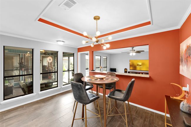 Dining space with a raised ceiling, wood finished floors, crown molding, a chandelier, and ceiling fan | Image 15