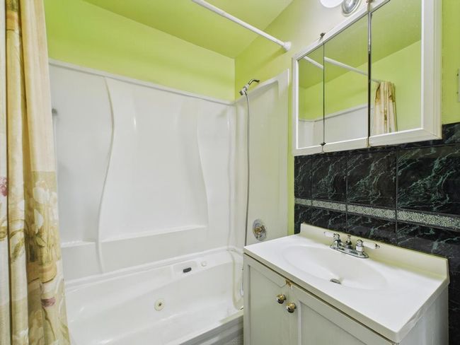 Bathroom with a combined bath / shower with jetted tub, vanity, and decorative backsplash | Image 25