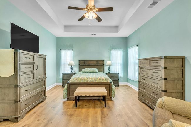 Bedroom with a raised ceiling, light wood-type flooring, baseboards, and visible vents | Image 11