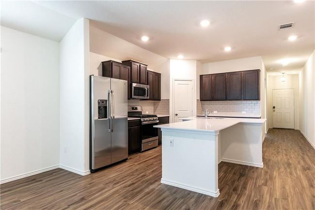 Kitchen featuring appliances with stainless steel finishes, dark wood-style flooring, light countertops, backsplash, and recessed lighting | Image 5