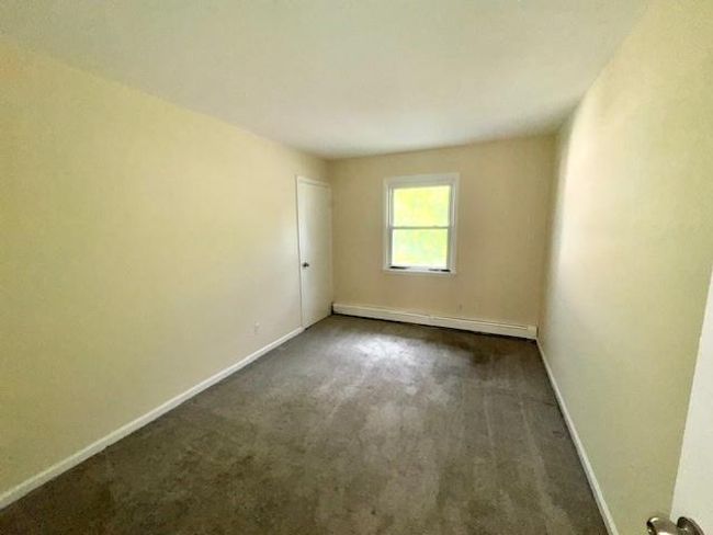 Empty room with a baseboard heating unit, baseboards, and dark carpet | Image 9