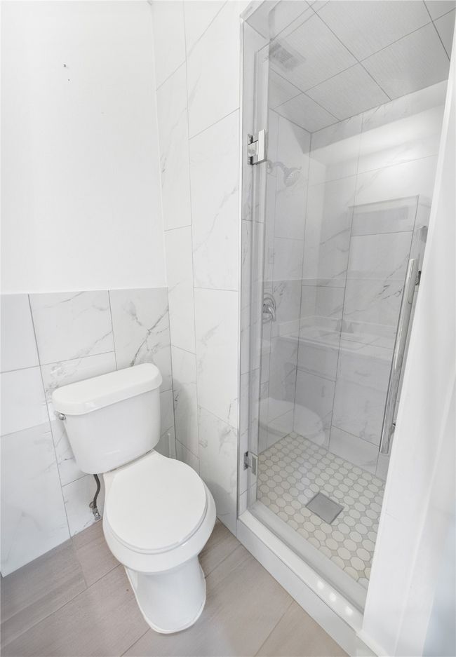 Bathroom featuring a tile shower, tile walls, and toilet | Image 14