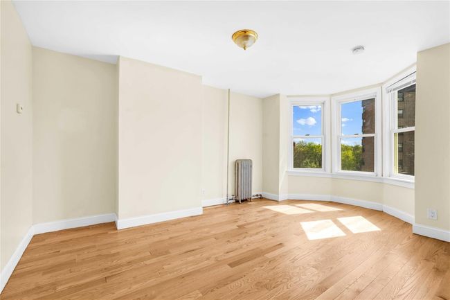 Unfurnished living room with radiator, light wood finished floors, and baseboards | Image 9