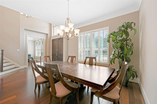 Elegant formal dining room with rich wood flooring, crown molding, and a statement chandelier. Plantation shutters provide natural light and privacy, creating a warm and inviting space for gatherings. | Image 4