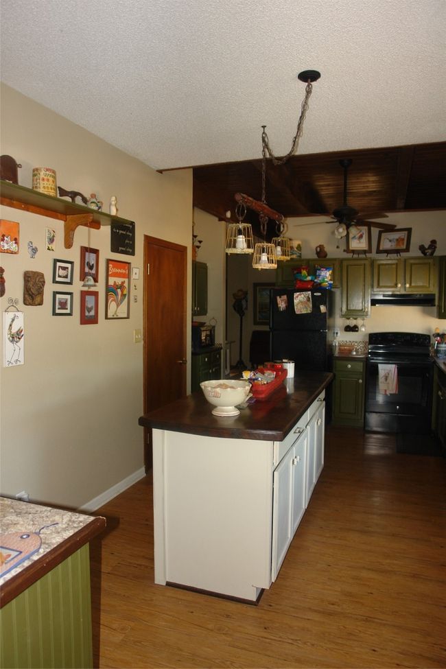 Kitchen featuring a textured ceiling, fridge, range hood, hardwood / wood-style floors, and stove | Image 7