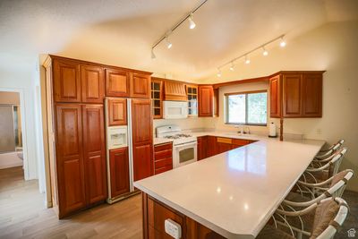 Kitchen with kitchen peninsula, a kitchen bar, white appliances, track lighting, and sink | Image 2