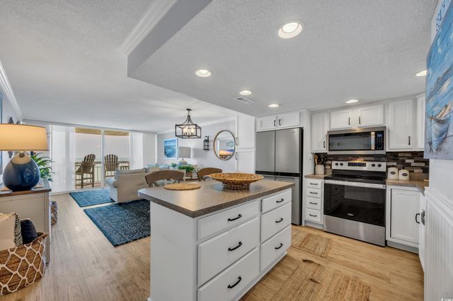Kitchen with appliances with stainless steel finishes, a textured ceiling, backsplash, white cabinets, and ornamental molding | Image 15