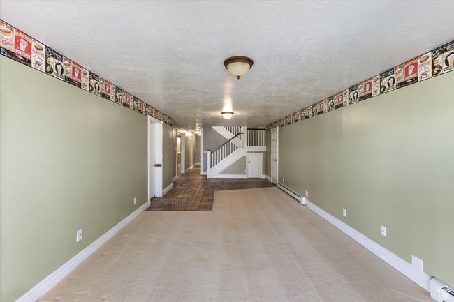 Empty room featuring carpet flooring, stairway, a baseboard heating unit, and baseboards | Image 26