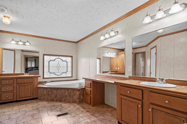 Bathroom with crown molding, two vanities, a garden tub, a textured ceiling, and tile patterned flooring | Image 32