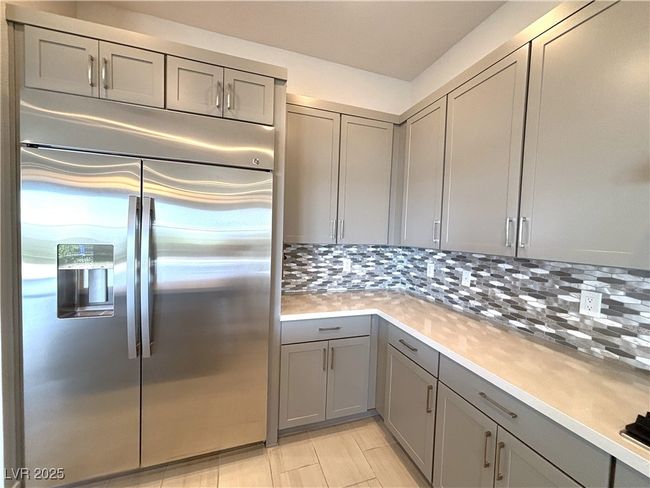 Kitchen featuring light tile patterned floors, light countertops, gray cabinets, stainless steel refrigerator with ice dispenser, and backsplash | Image 15