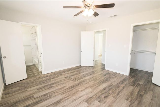 Unfurnished bedroom with wood finished floors, a closet, a walk in closet, connected bathroom, and a ceiling fan | Image 9