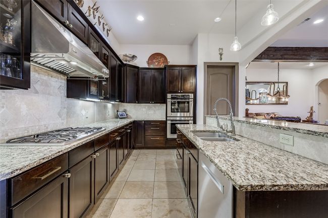 Kitchen featuring under cabinet range hood, light stone counters, appliances with stainless steel finishes, arched walkways, and a sink | Image 9