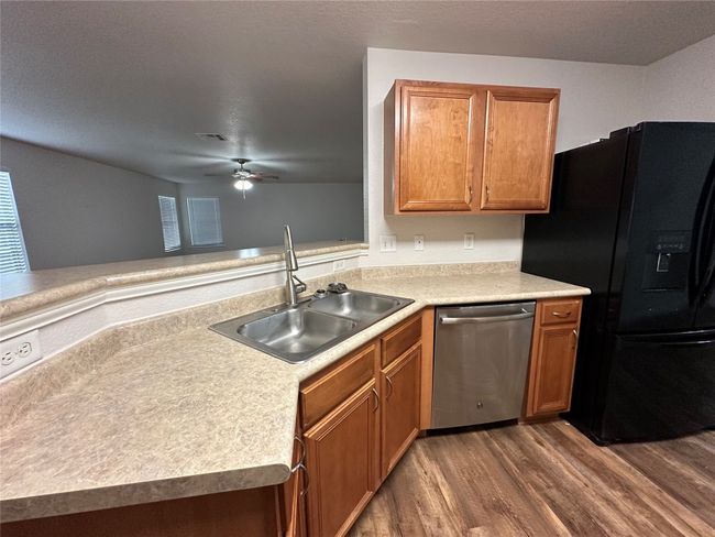 Kitchen with wood finished floors, black fridge, a ceiling fan, stainless steel dishwasher, and light countertops | Image 15